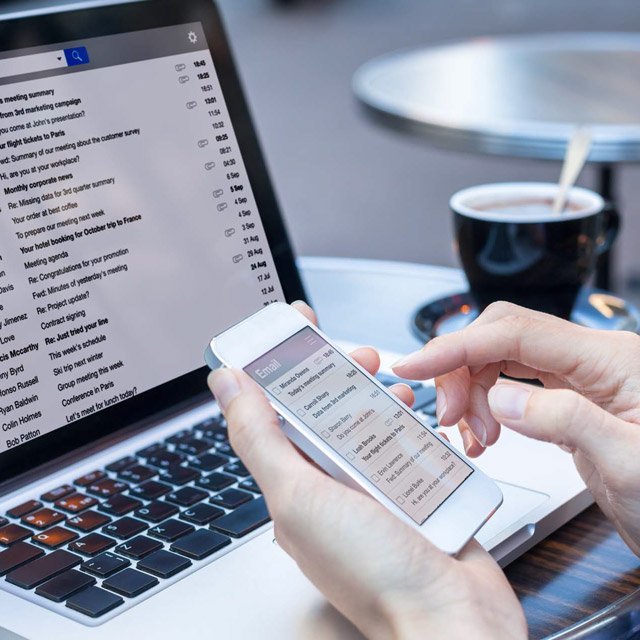 Person checking emails on phone and desktop at cafe table
